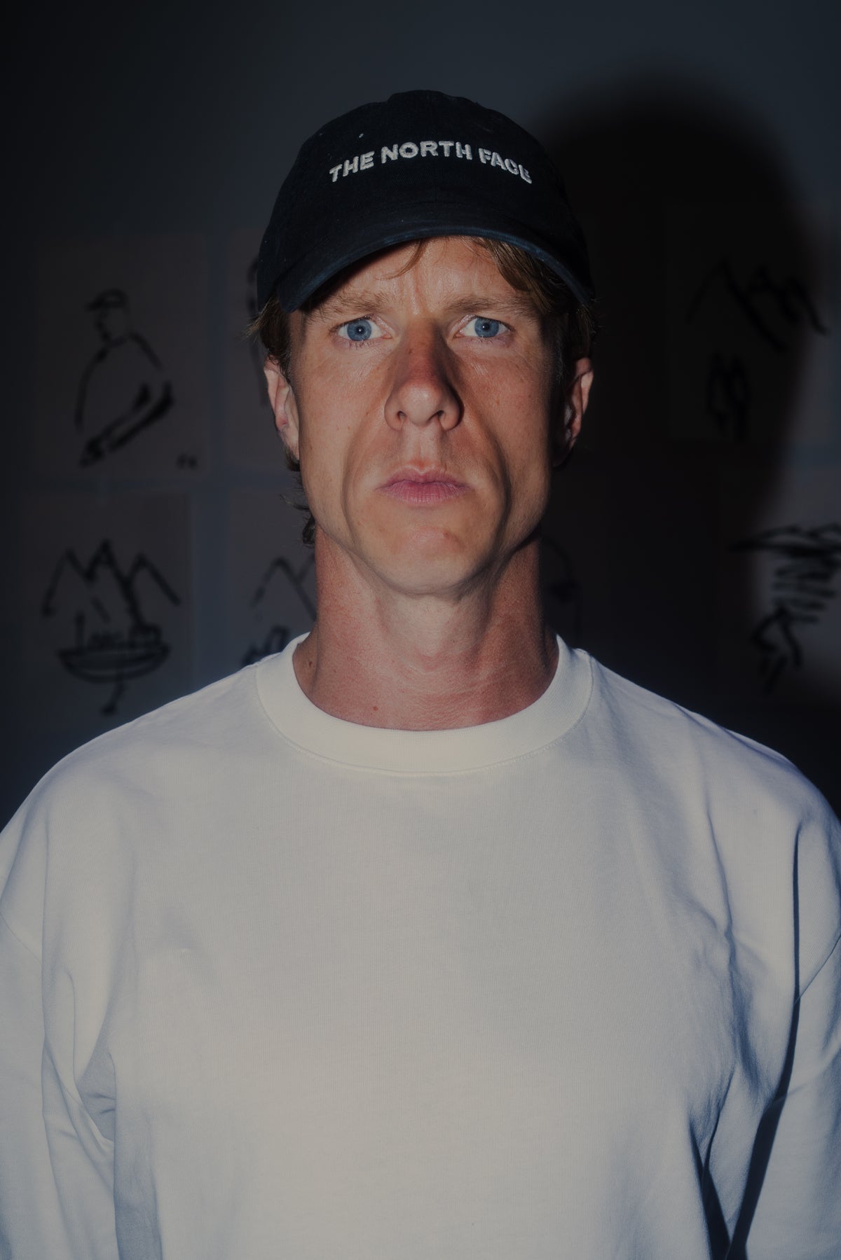 Man wearing a black cap with 'The North Face' logo against a dark background